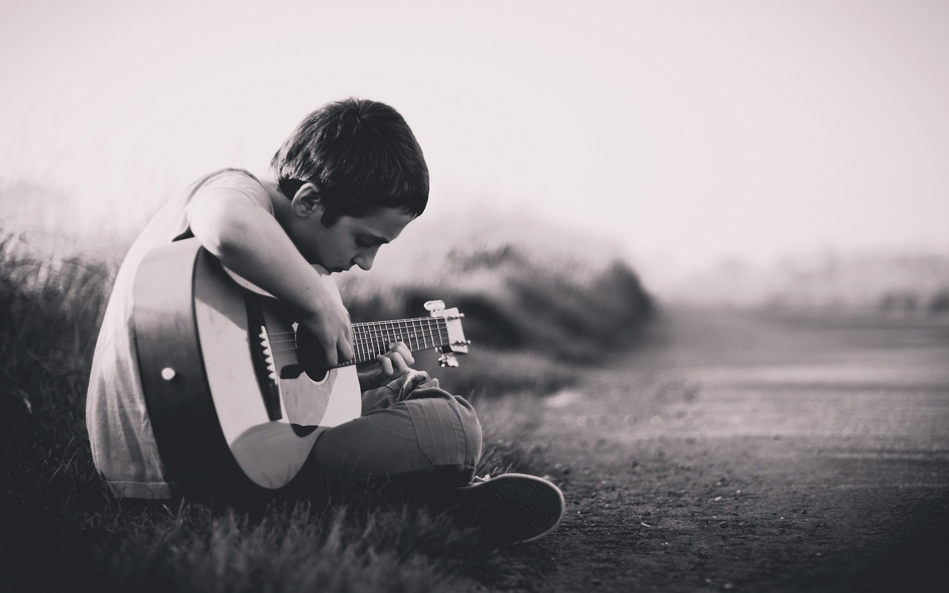 sepia-toned photo of boy playing guitar by side of rural road
