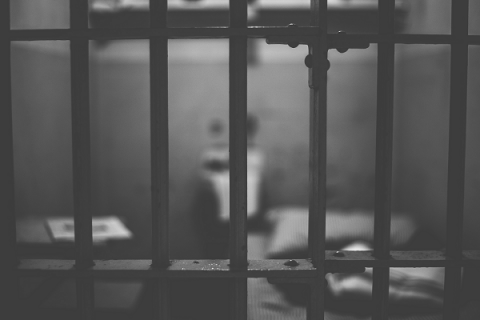 Black and white picture of empty prison cell seen through bars. Only the bars are in focus.